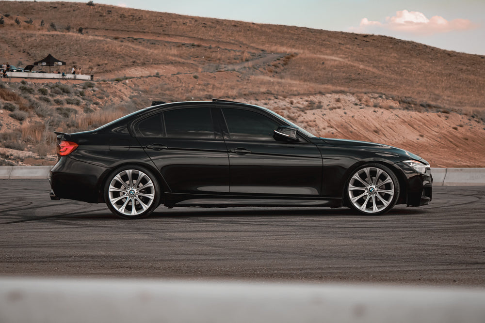 Black sedan with dark side windows parked beside a dry hillside.